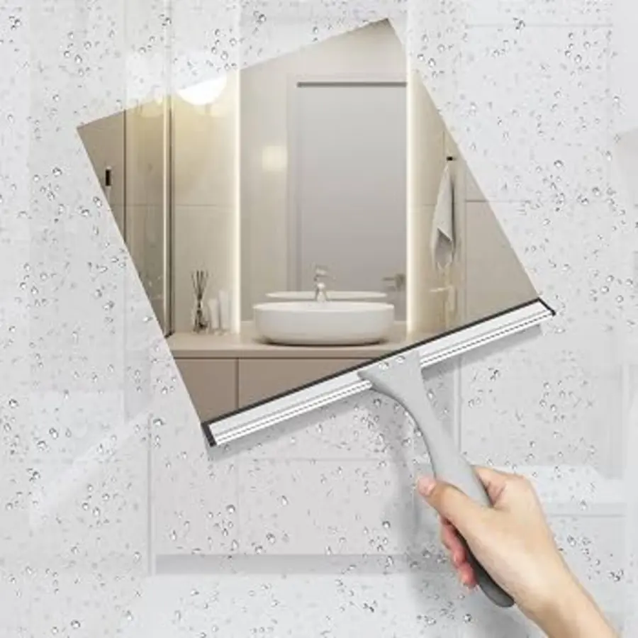 A hand using a squeegee on a bathroom mirror with water droplets.