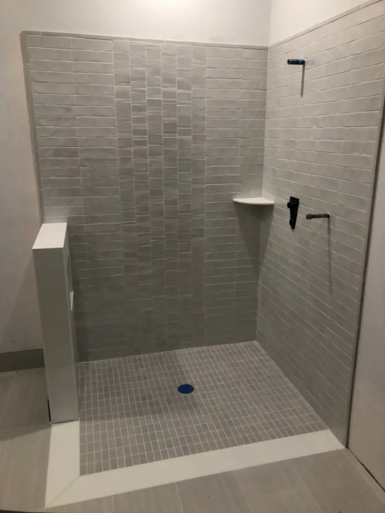 Curbless shower with grey tiles and a floor drain, no bath mat present.