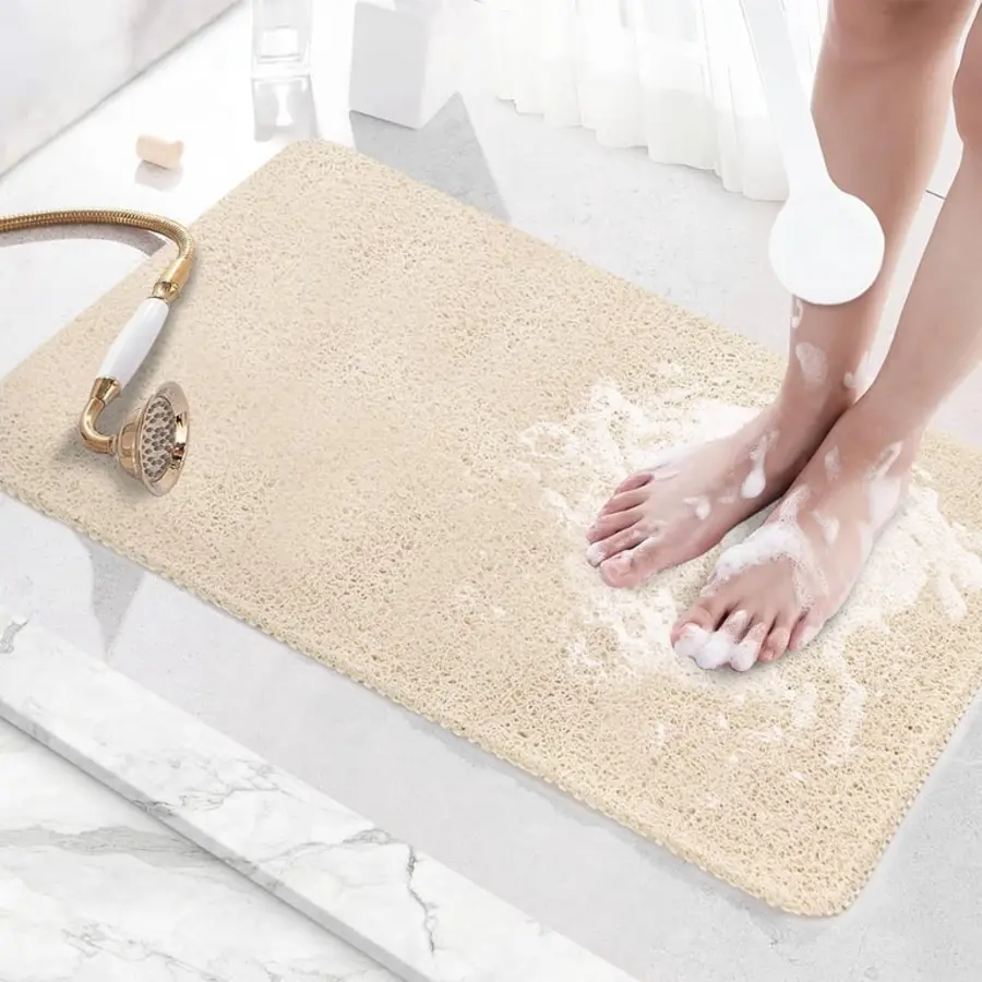 Bath mat on a stone floor with wet feet applying soap, showerhead nearby.