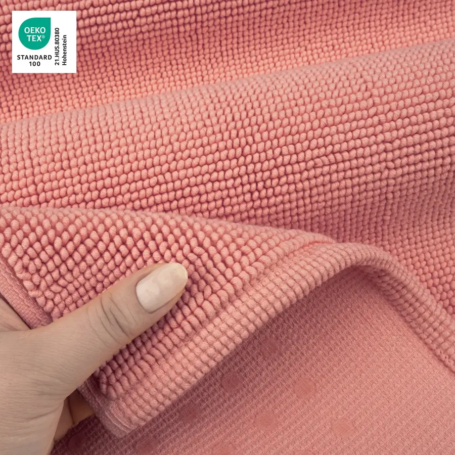 A hand holding a folded pink textile bath mat showing textured fabric.