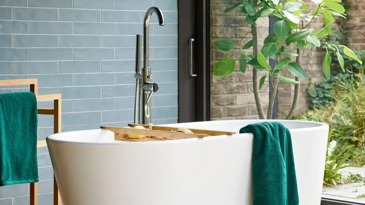 Modern bathroom featuring a freestanding tub, wooden tray, and neatly arranged teal bath towels.