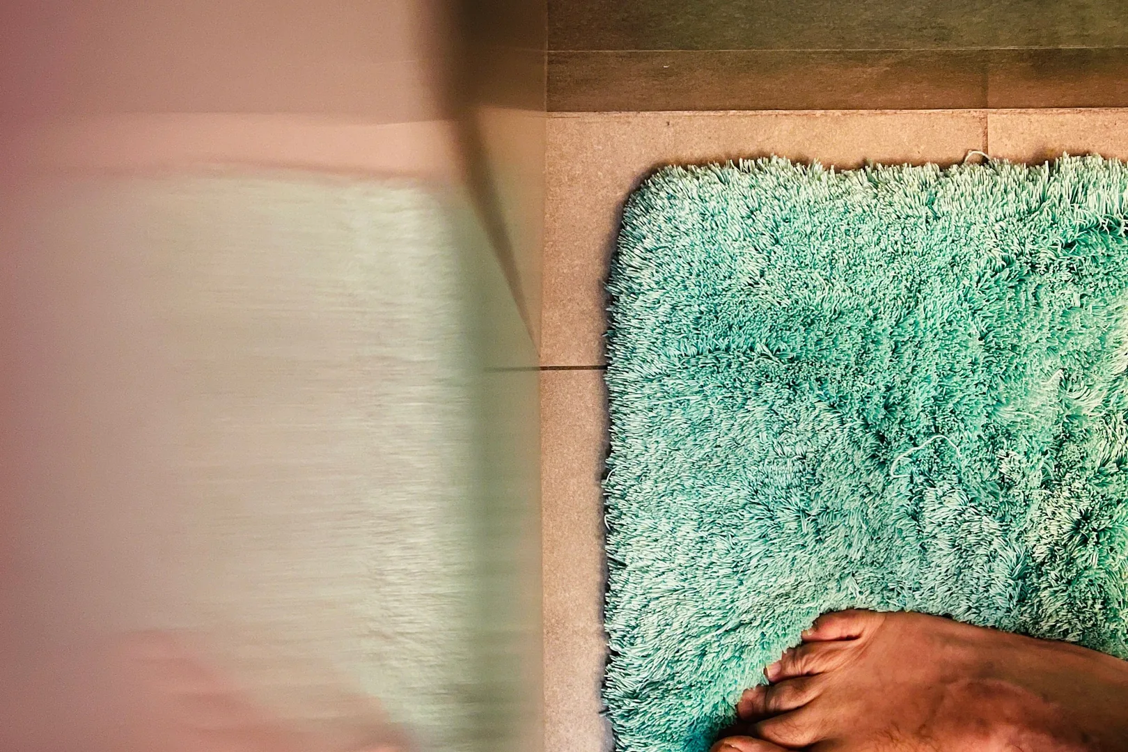 Bare feet standing on a green bath mat over a tiled bathroom floor.