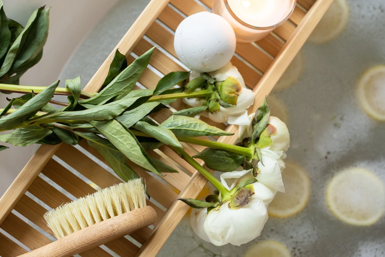 Bath bomb and spa items arranged on a wooden tray beside bath water.