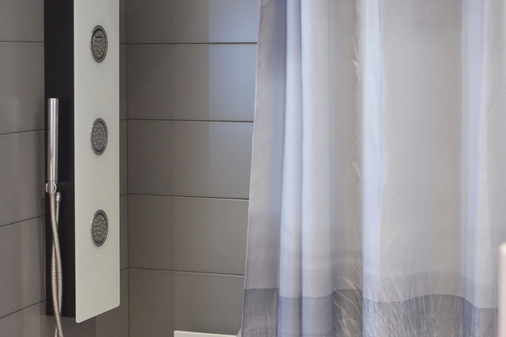 White shower curtain hanging beside a tiled shower enclosure.