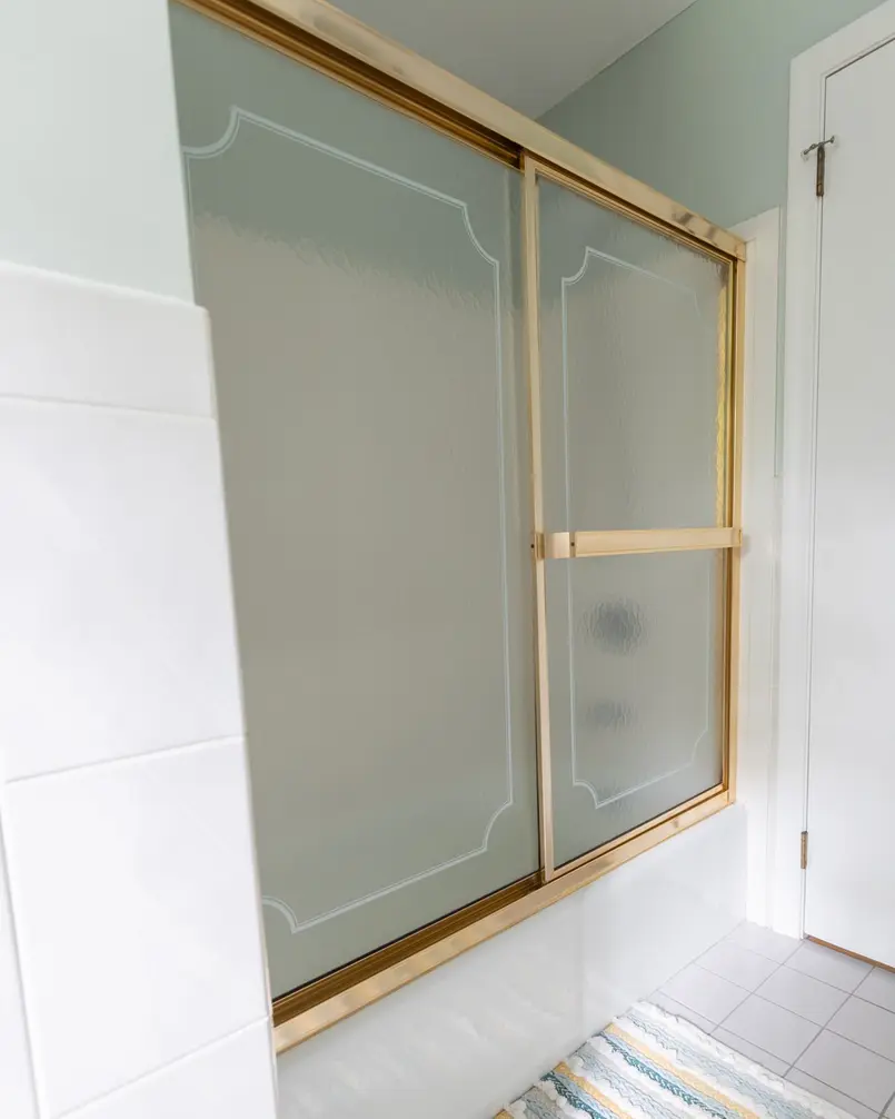 Sliding shower door with gold frame and textured glass on a tiled floor.