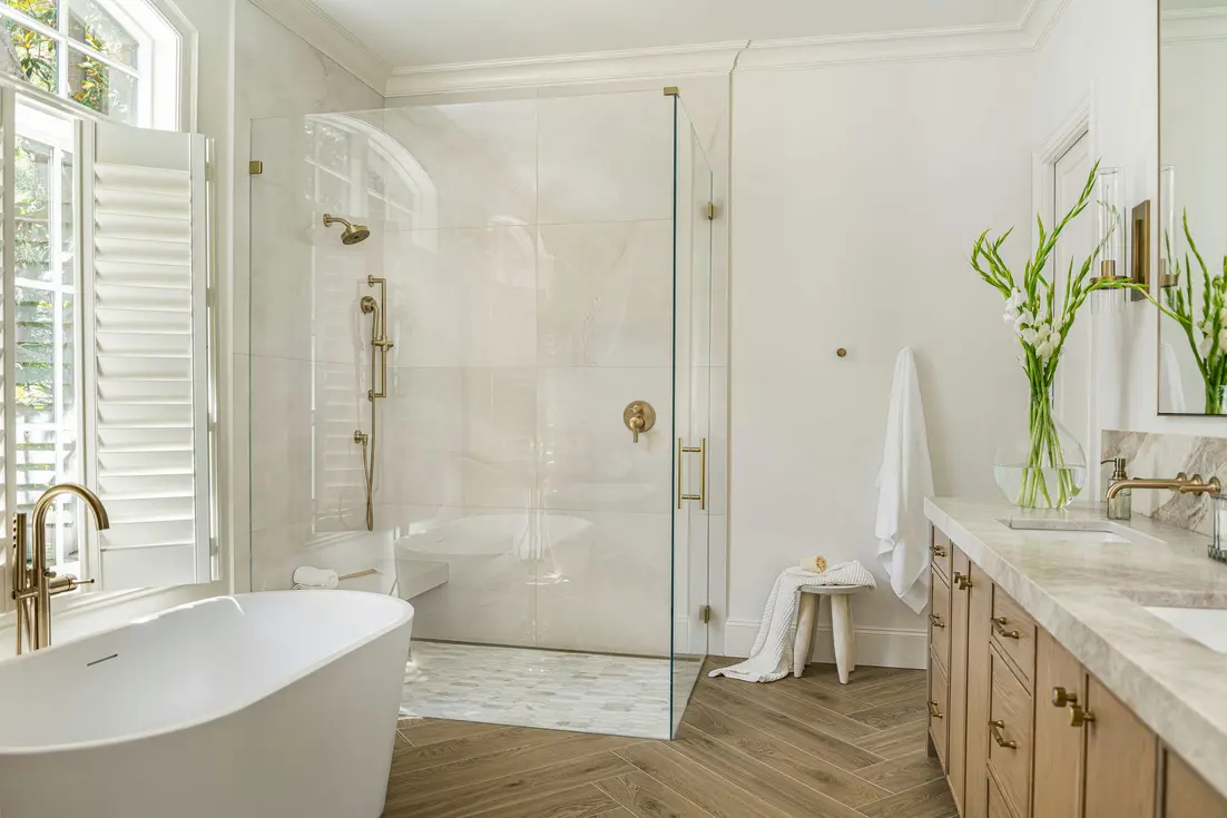 Modern bathroom featuring a curbless shower, freestanding tub, dual sinks, and natural light.