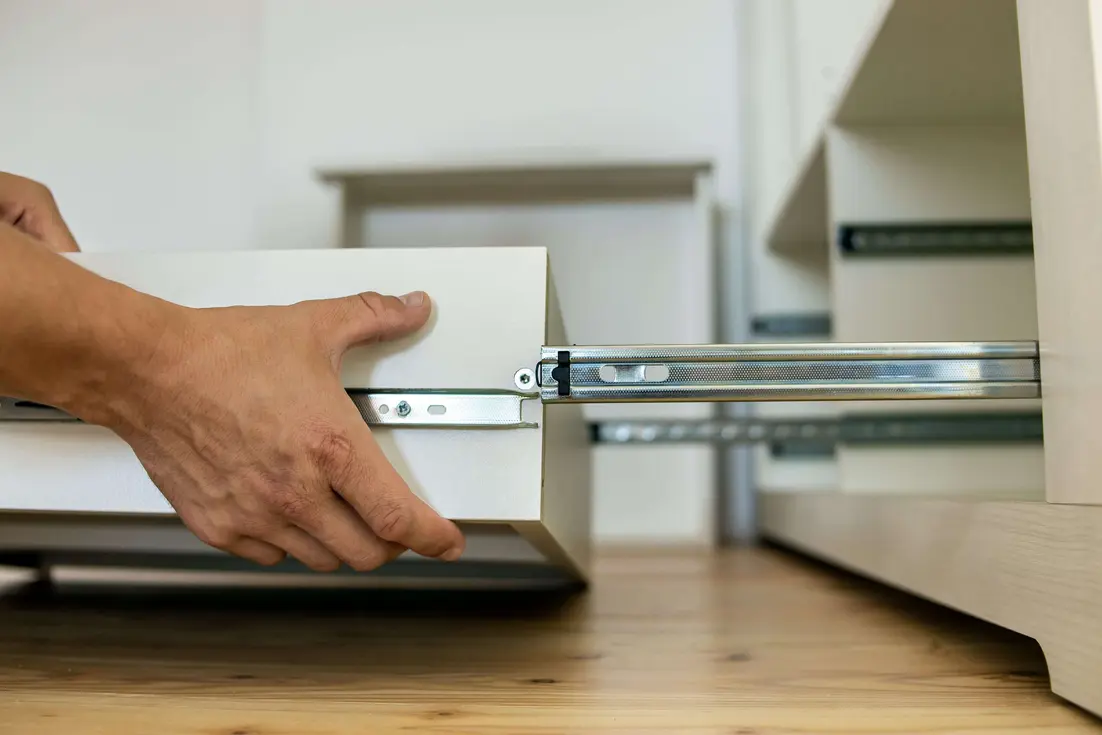 A hand is positioning a drawer along metal slides within a cabinet.