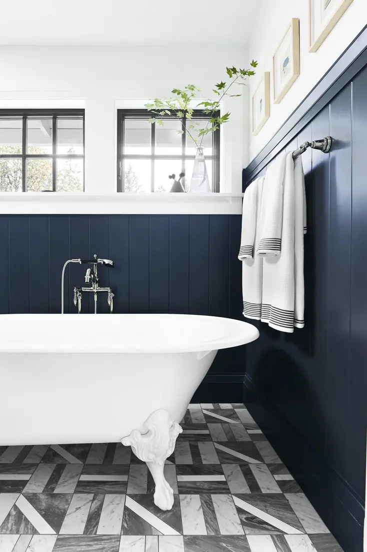 Hanging towels on a rod near a freestanding bathtub with dark blue walls and patterned floor tiles.
