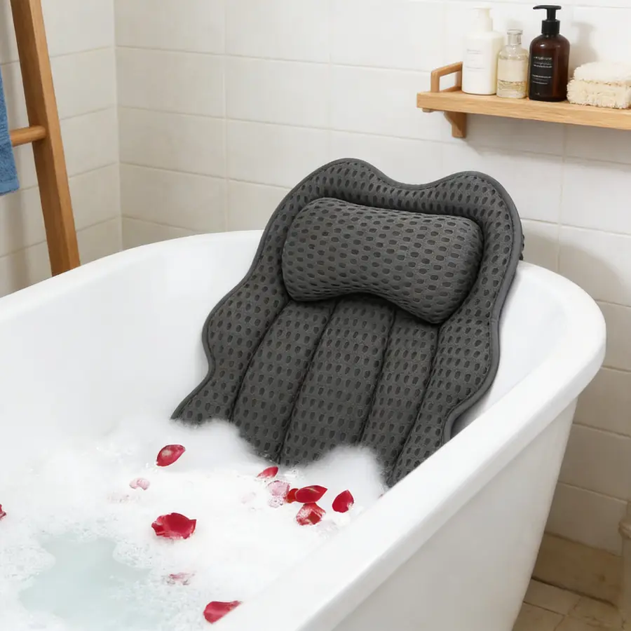 A gray bath pillow is resting in a bathtub with bubbles and rose petals.