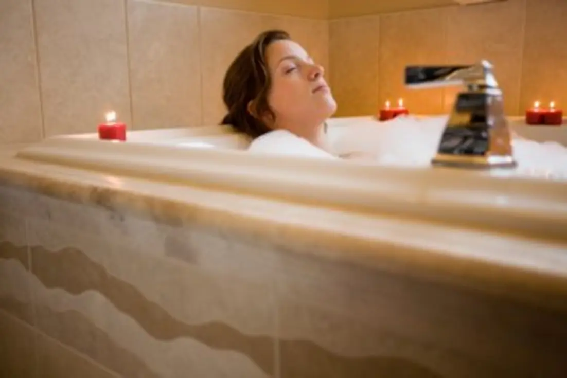 A person relaxes in a bubble-filled bathtub surrounded by lit candles.