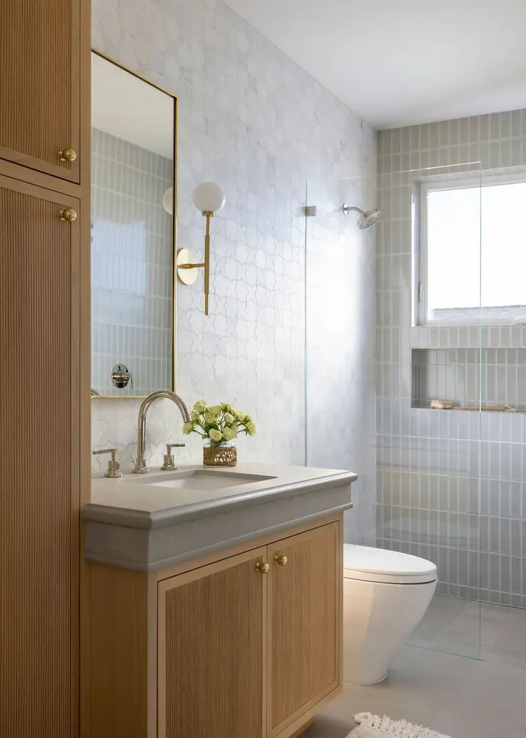 Modern small bathroom with a toilet, vanity, and glass shower, featuring neutral tiles and wood cabinetry.
