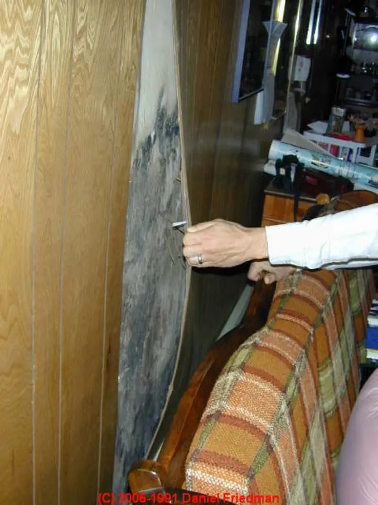 A hand tests a cleaning solution on a concealed area of wooden wall.