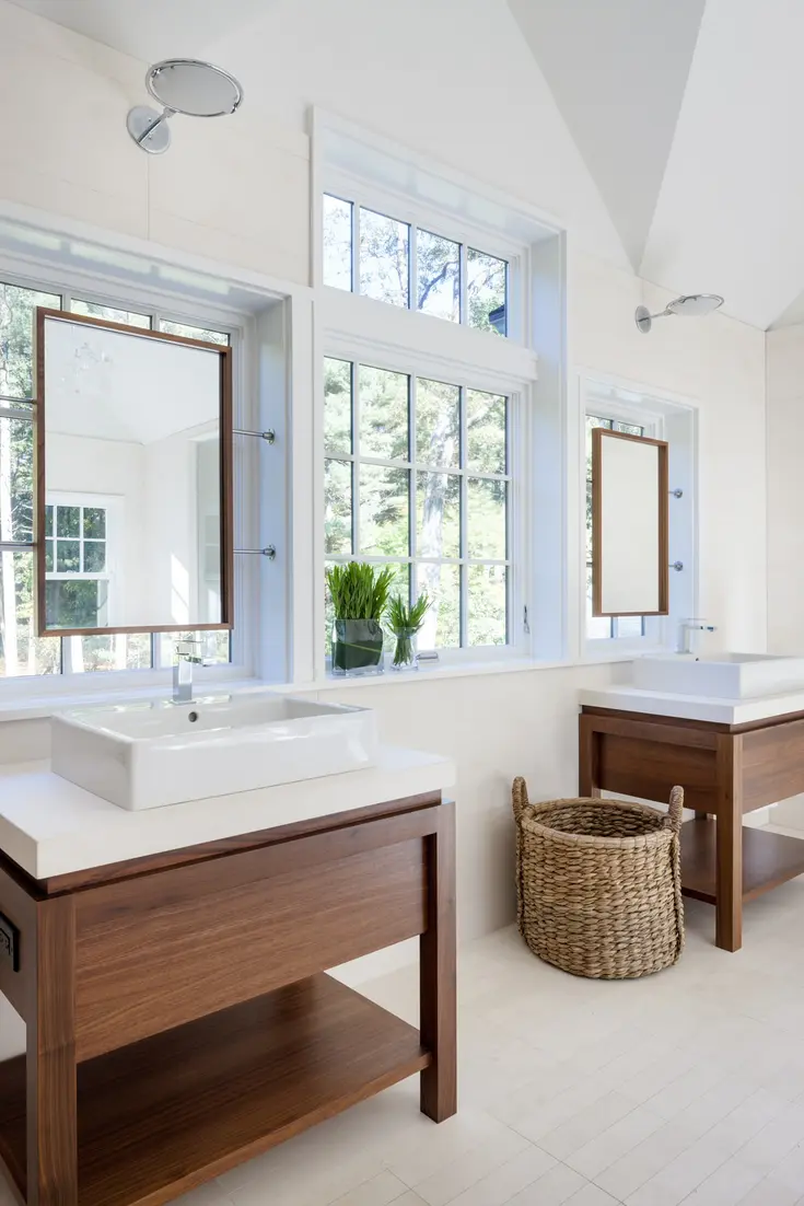 Bright bathroom featuring dual vanities, modern sinks, and mirrors above, with a view of greenery outside.