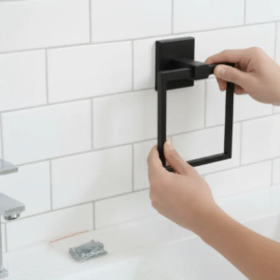 Person holding a black towel ring against white tiled wall for installation.