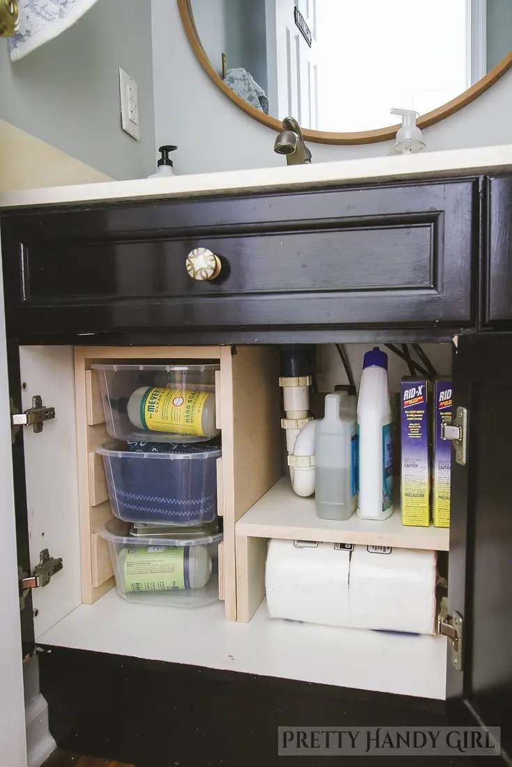 Under-sink cabinet with organized cleaning supplies and storage containers around plumbing.