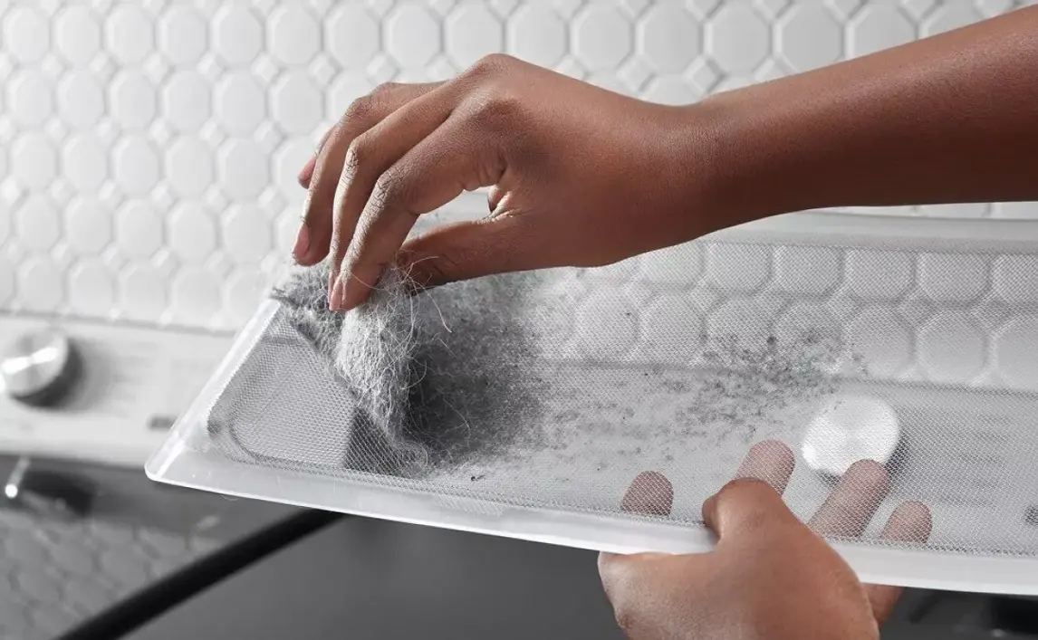 A hand removes lint from a dryer lint filter.