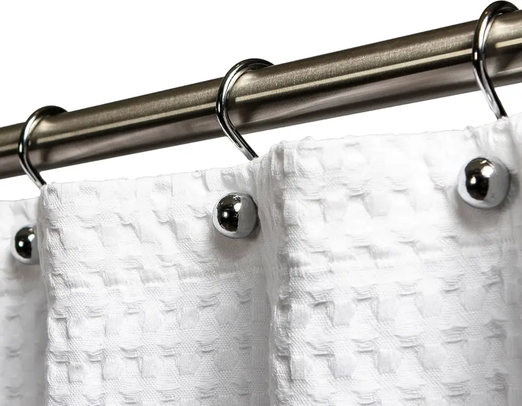 Close-up of white shower curtain fabric with metallic hooks attached to a rod.