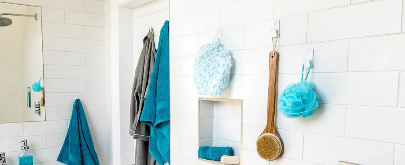 A bathroom scene featuring adhesive towel hooks on a white tiled wall.