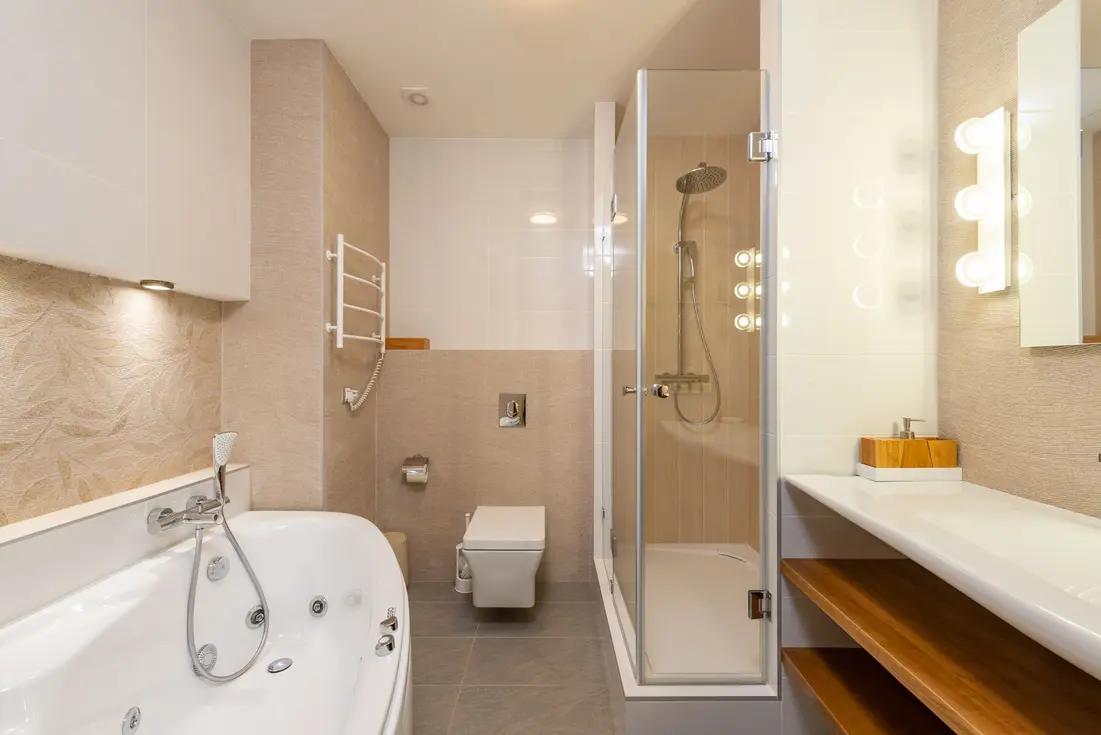 Modern bathroom featuring a bathtub, shower, toilet, and vanity with lights.