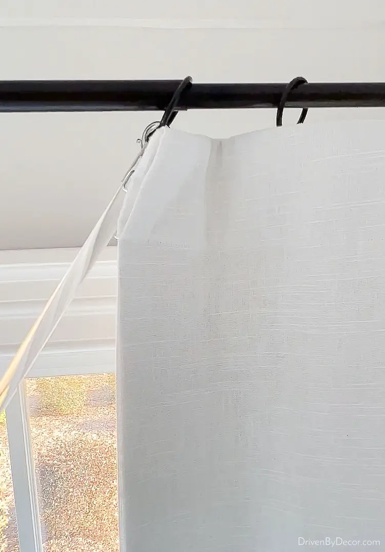 Close-up of a white curtain panel on a telescoping rod with curtain rings.