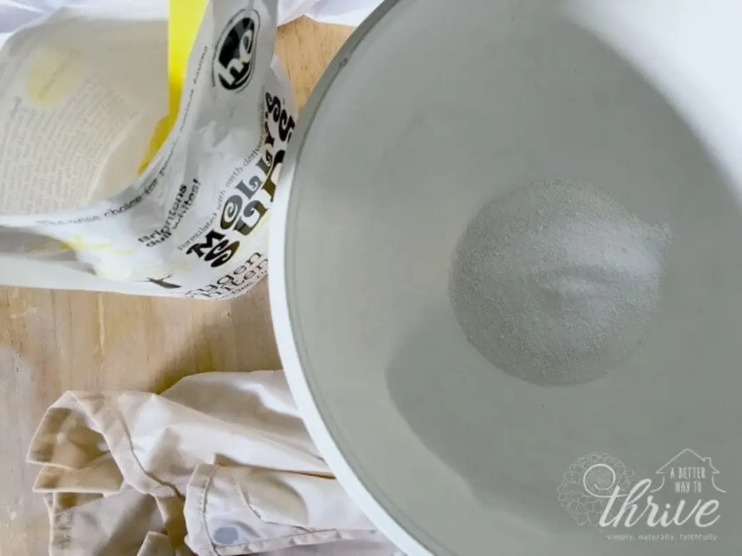 A white bowl with white powder inside, next to an open bag and fabric.