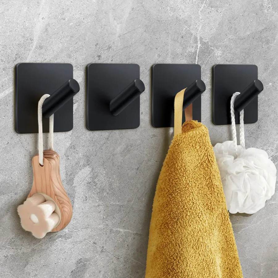 Four black wall hooks holding a yellow towel and two bath accessories on a grey background.