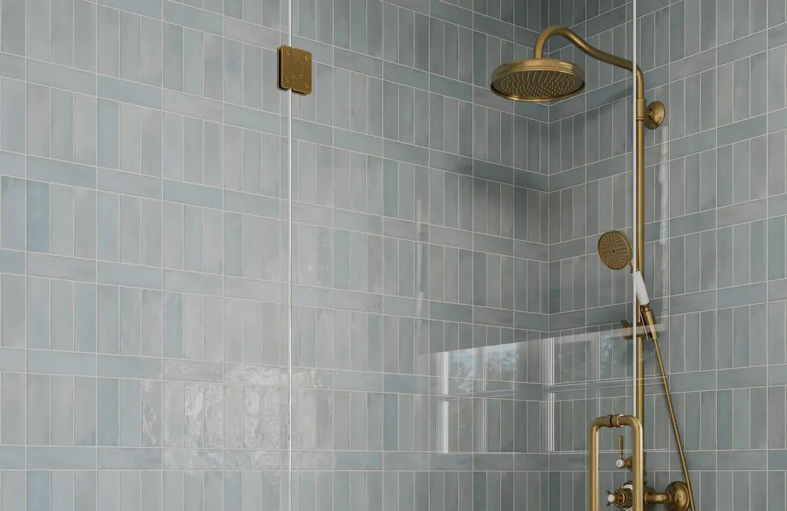 A shower featuring blue subway tiles and a brass shower fixture.