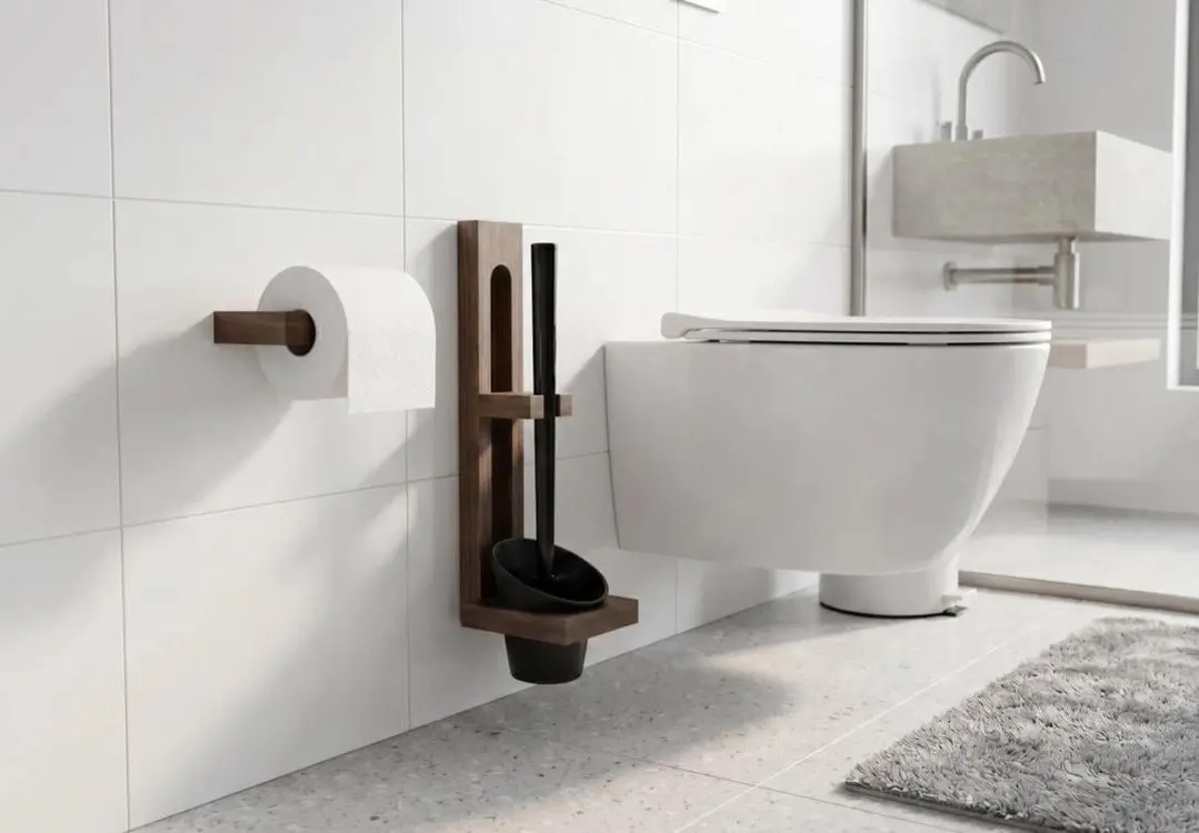 Wall-mounted toilet brush holder beside a white toilet and a roll of toilet paper on a wall.