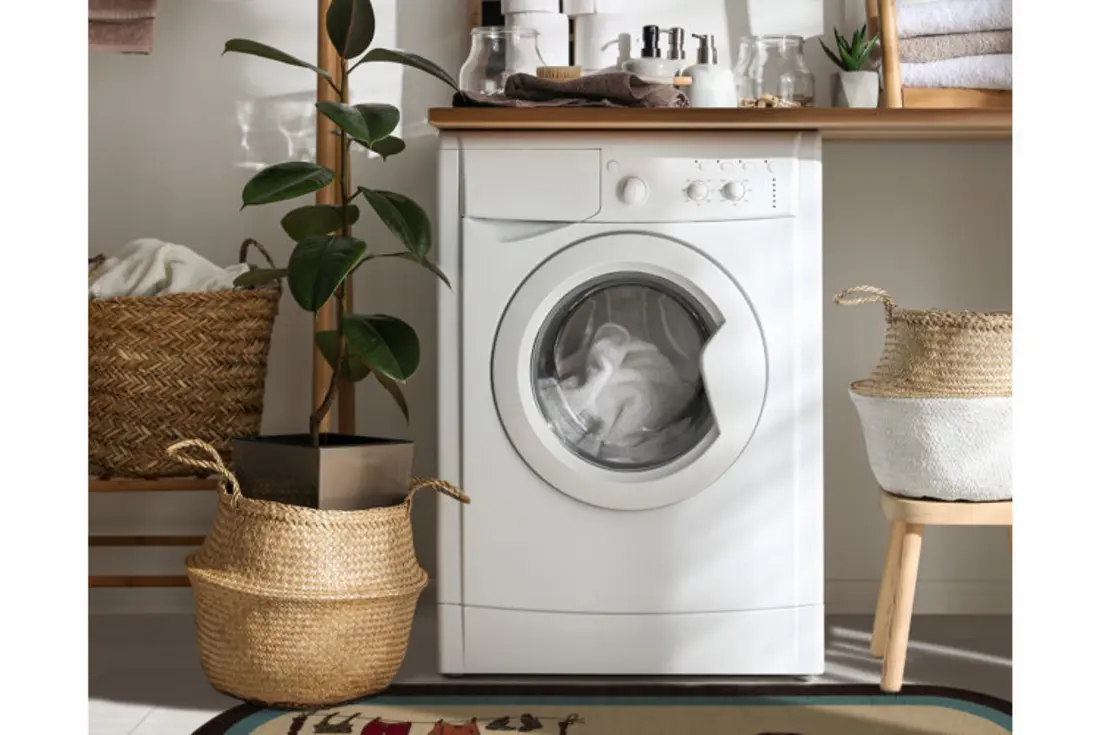 A washing machine with towels inside and woven baskets nearby in a laundry area.
